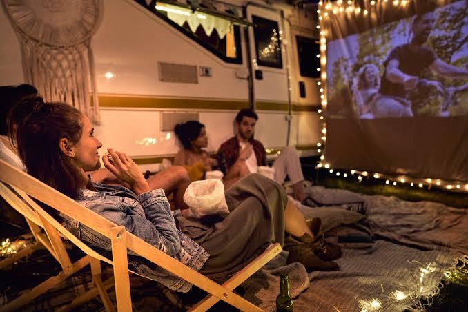 Campers watching an outdoor movie under string lights