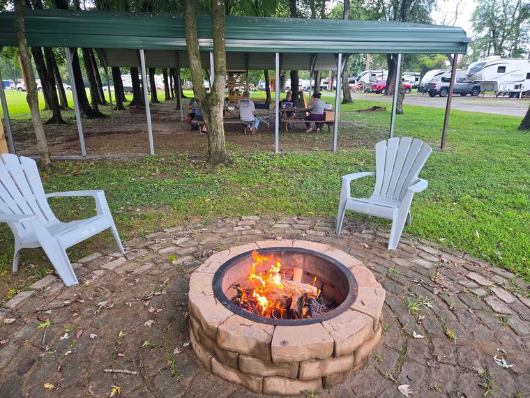 A stone fire pit burning between two Adirondack chairs under the pavilion