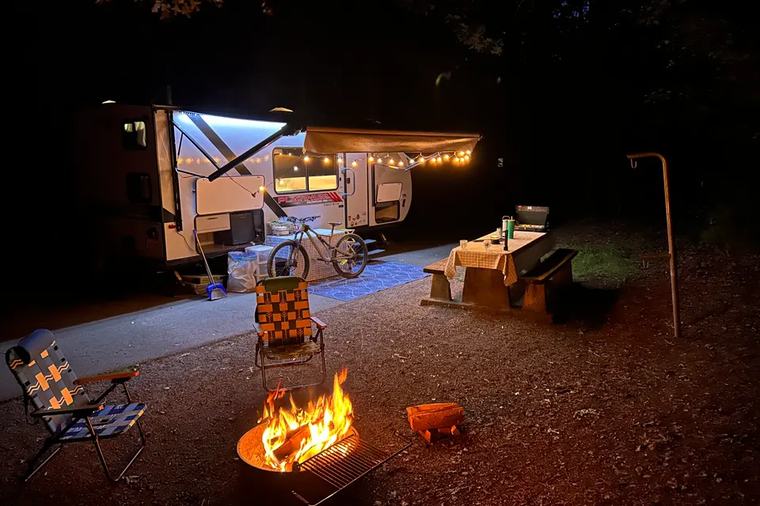 An RV lit with string lights beside a campfire after dark