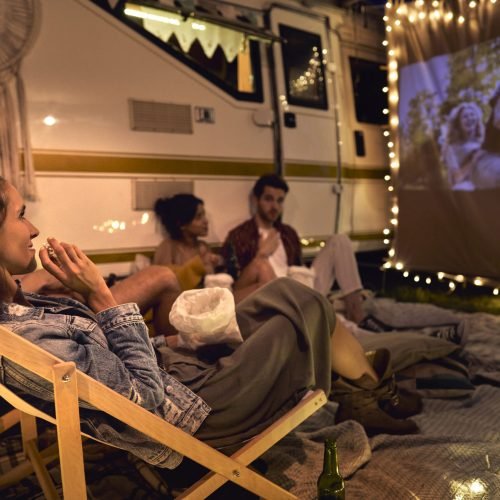 Young cheerful people watching a movie on camping site